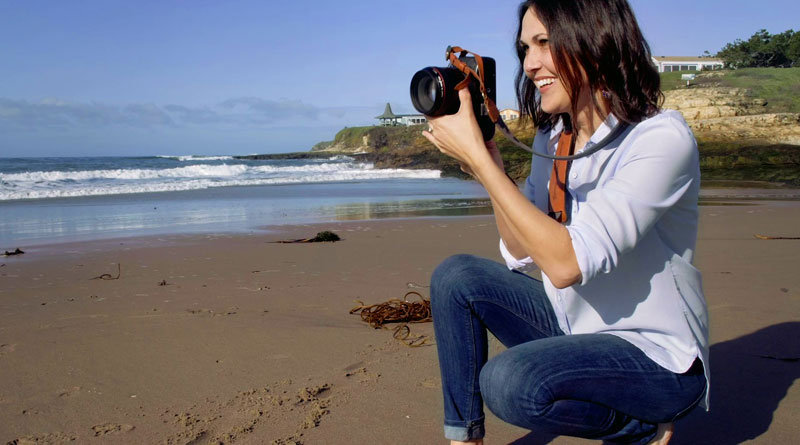 Smiling Photographer aiming camera on beach
